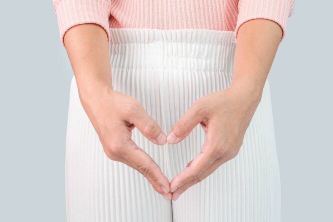 Hands form a heart shape in front of a pink sweater and white pleated skirt.