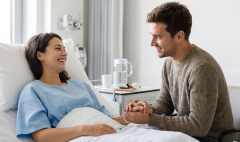 image 32-1 Man sits beside a woman in a hospital bed, holding her hands and offering support.